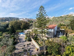 Eine Villa an einem Hügel mit einem Schwimmbad, Steinmauern und einem Garten mit verschiedenen Pflanzen.