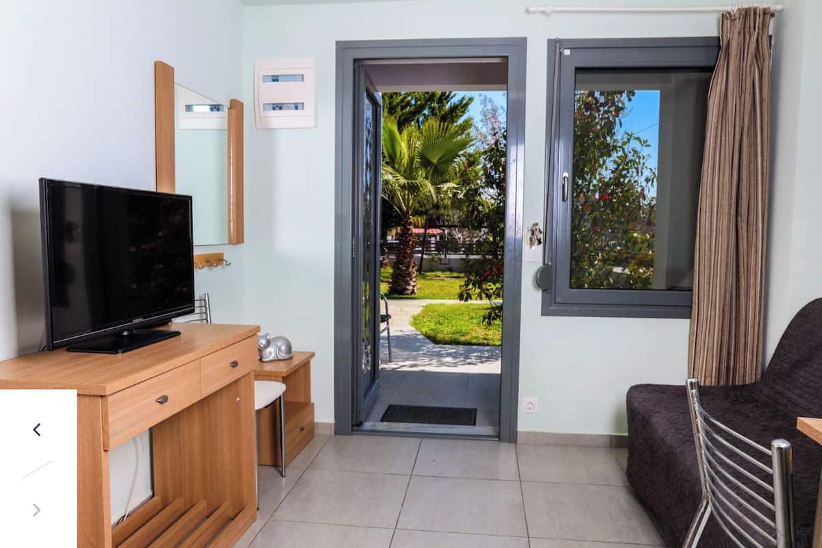 A modern room with a flat-screen TV on a wooden desk, a sofa, and a door leading to a garden.
