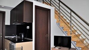 A modern kitchen with dark cabinets, a black countertop, and a built-in stove. There's a wooden staircase with metal railings and a TV on a wooden stand. - Aquarius Nikiti (Nikiti)