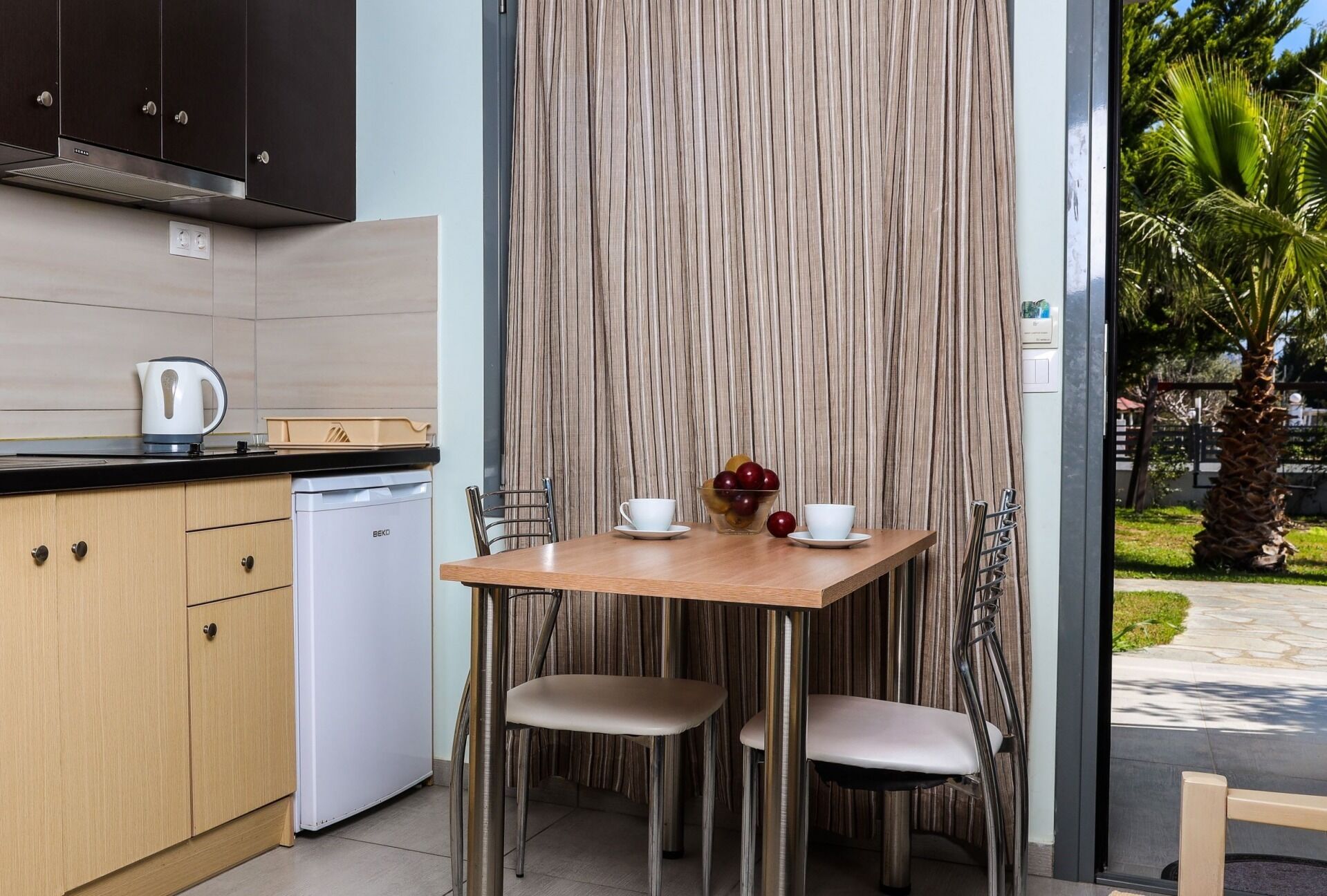 A compact kitchen with a kettle, a small refrigerator, and a dining area with a table and chairs.