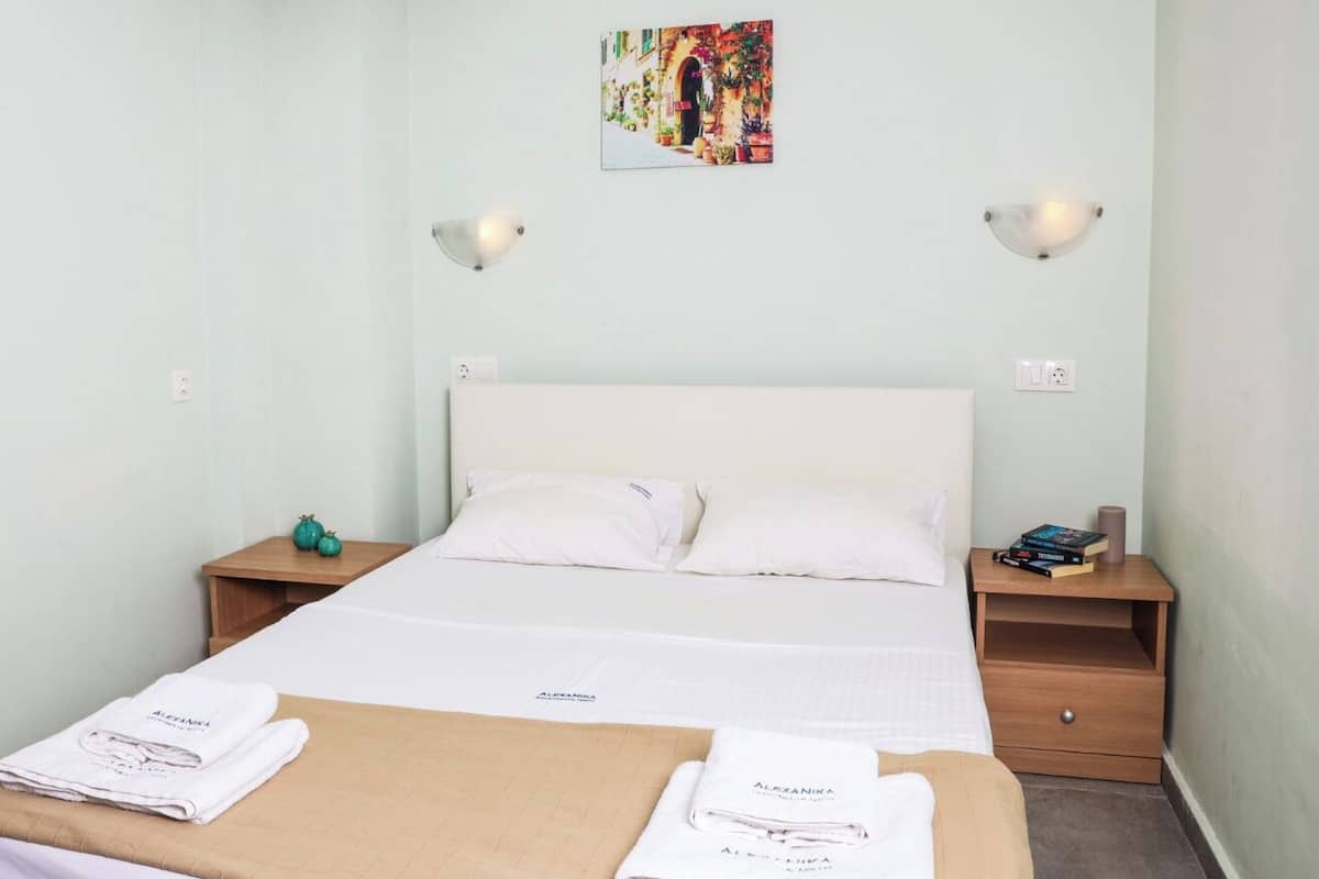A neatly made bed with white linens and pillows, two bedside tables with lamps, a small artwork on the wall, and a neatly folded towel on the bed.