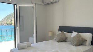 A hotel room with a bed, a nightstand, a lamp, and a view of the sea.