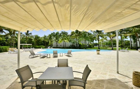 A covered outdoor area with a pool, lounge chairs, and tables.
