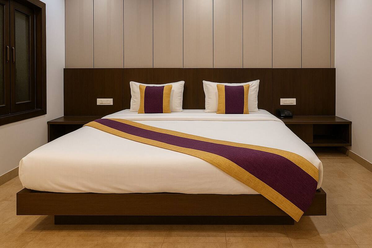 A hotel room with a large bed, two nightstands, a wooden headboard, and a window with blinds.
