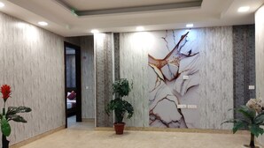 A spacious lobby with marble walls, a large mural, and potted plants. - Hotel Rajvansh Palace (Gurugram)