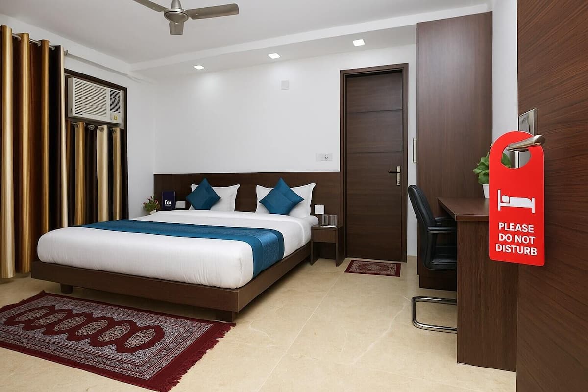 A hotel room with a bed, bedside table, a desk with a chair, a red 'Please do not disturb' sign, a ceiling fan, and a window with curtains.