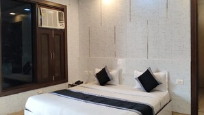 A bedroom with a bed, a window, a wardrobe, and an air conditioning unit. - Hotel Rajvansh Palace (Gurugram)