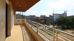 A balcony with a metal railing, a view of the cityscape, and a building with multiple floors. - Hotel Rajvansh Palace (Gurugram)