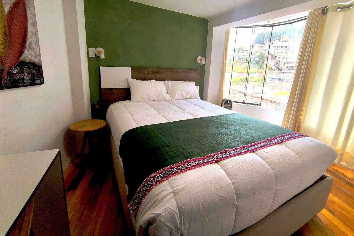 A neatly made bed with a green headboard, a bedside table, and a window with curtains.