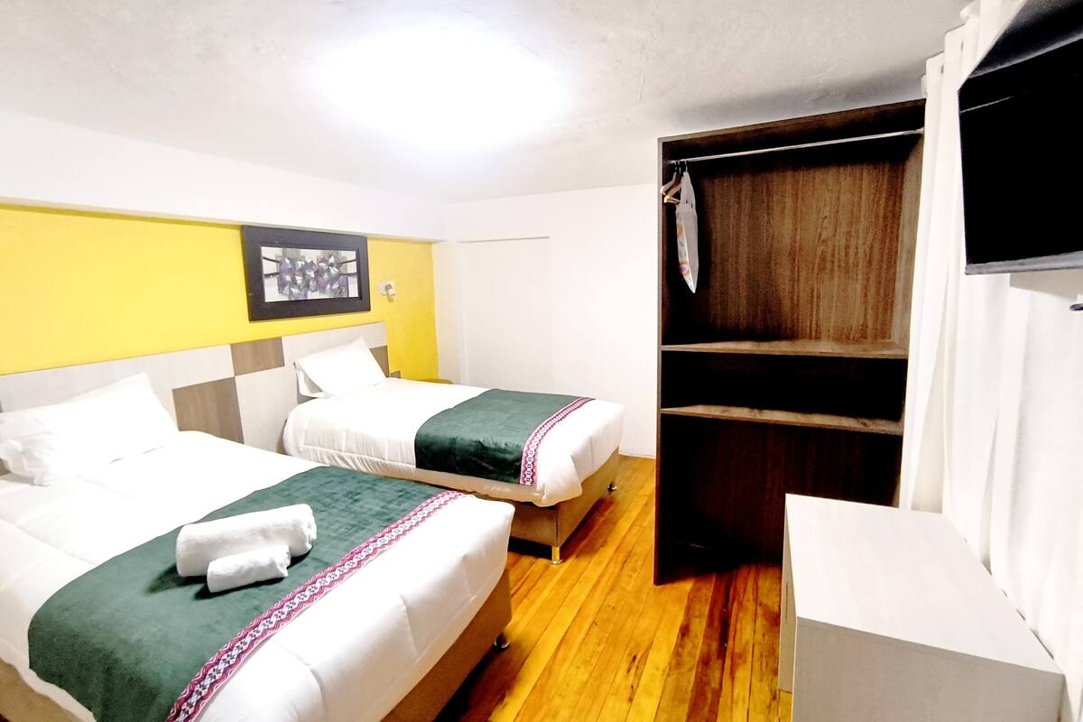 A hotel room with two beds, a wooden wardrobe, a television, and a framed picture on the wall.