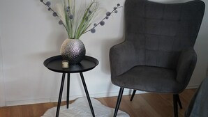 Ein modernes Zimmer mit einem grauen Polsterarmlehnstuhl, einem kleinen schwarzen Tisch mit einer dekorativen Vase und Kerze sowie einem weißen, flauschigen Teppich.