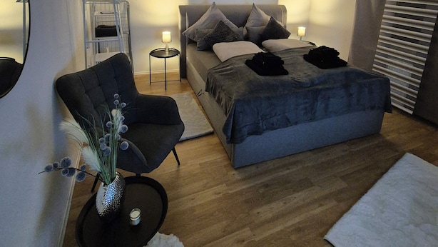 Ein modernes Schlafzimmer mit einem Bett, einem Sessel, einem kleinen Tisch und einem Bild an der Wand.