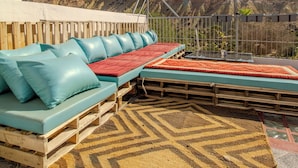 Une terrasse sur le toit, avec un long banc, un tapis à motifs et une vue sur un paysage vallonné.