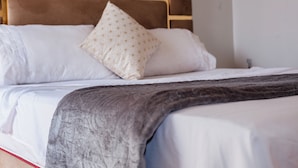 Un lit bien fait, avec une couverture grise, des oreillers blancs et un coussin décoratif.