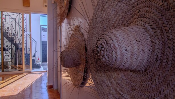 Un couloir orné d’une œuvre d’art murale en fibres tissées, une porte en verre donnant sur l’extérieur et un sol carrelé.