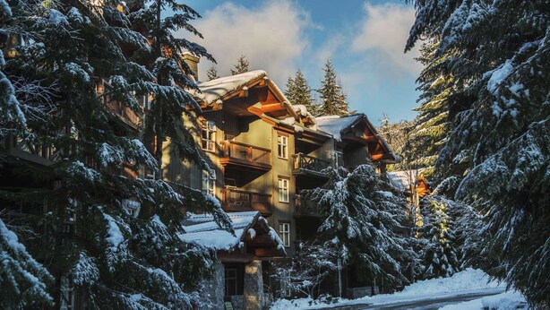 A multi-story lodge with a wooden exterior, surrounded by snow-covered trees.