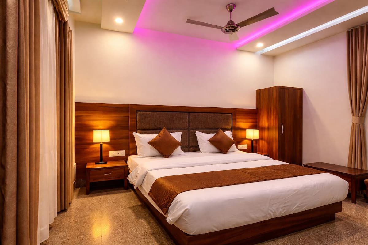 A hotel room with a large bed, wooden headboard, two bedside tables with lamps, a wardrobe, and a ceiling fan.