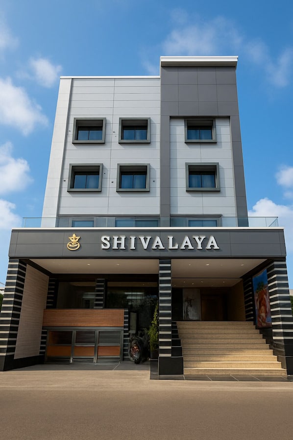 A modern hotel named SHIVALAYA with a clean, contemporary design, featuring a prominent entrance with steps and a large sign.