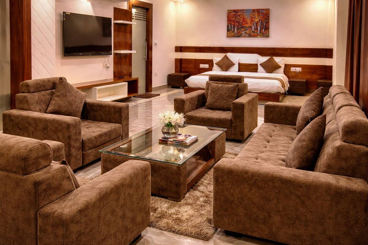 A modern hotel room with a large bed, a TV, and a seating area with sofas and a coffee table.