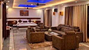 A modern hotel room with a king-sized bed, a sofa set, a coffee table, and a ceiling fan. - Hotel SHIVALAYA by GPH (Haridwar)