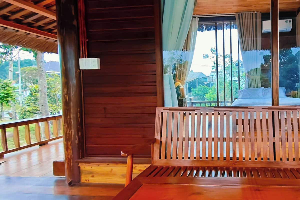 A wooden cabin with a bed, a wooden bench, and a view of the surrounding greenery.