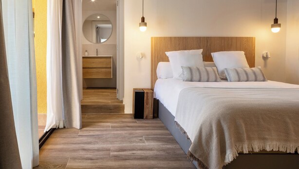 Ein Schlafzimmer mit einem Holz-Kopfteil, einem großen Bett mit weißer Bettwäsche, einem Nachttisch und einem Spiegel über dem Waschbecken.