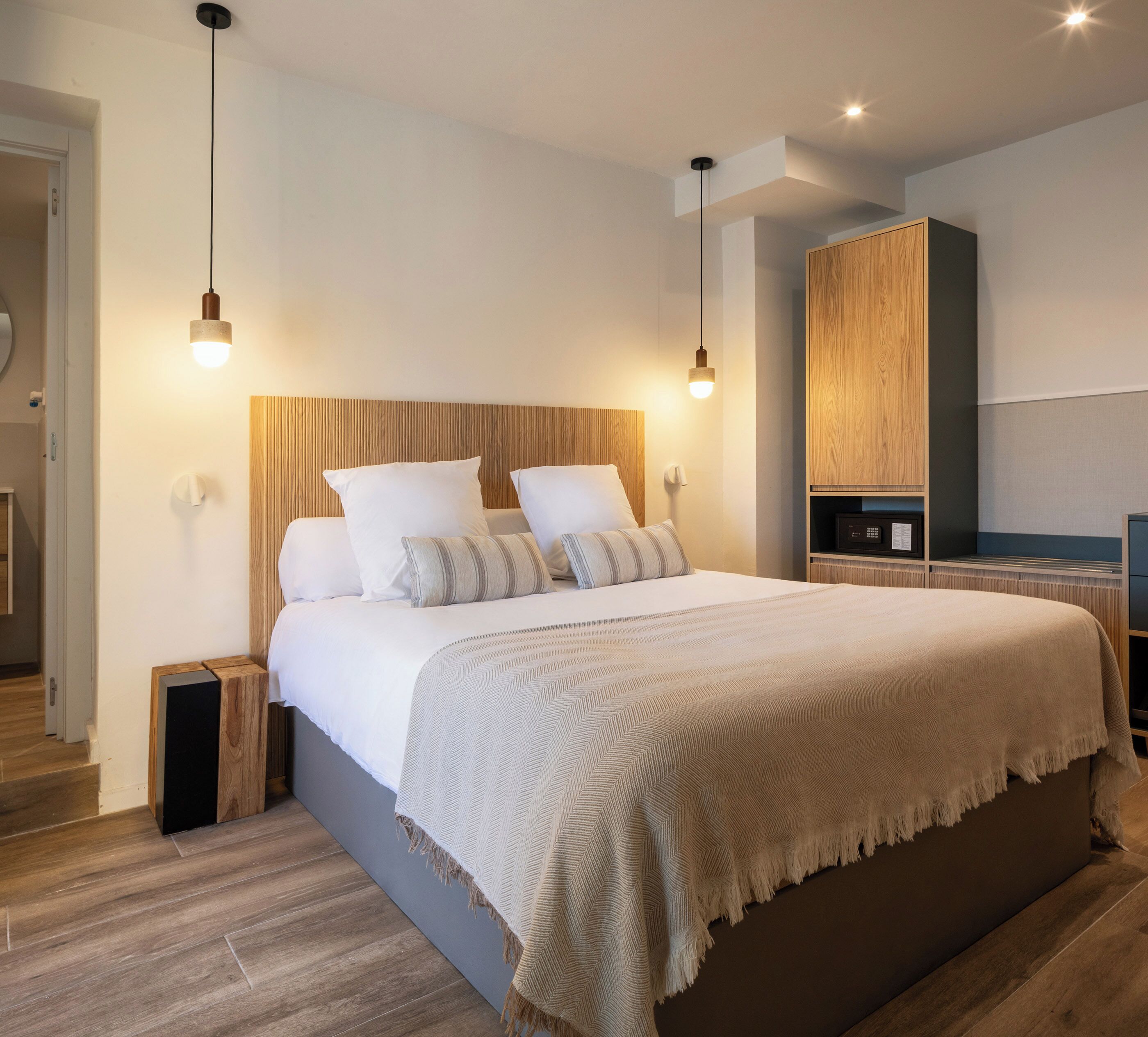 Une chambre à coucher moderne avec un grand lit, une tête de lit en bois, des tables de chevet et une armoire intégrée.
