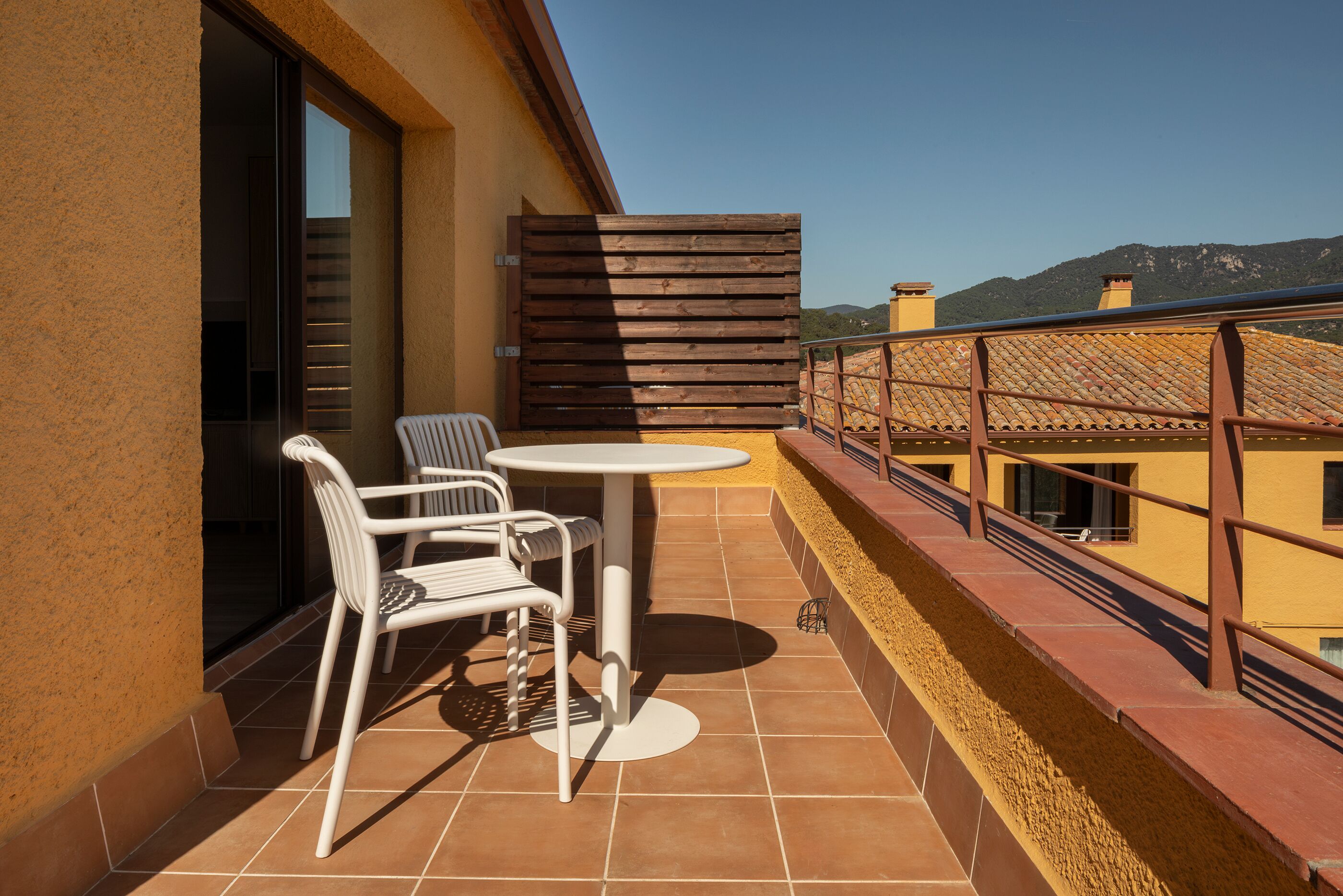 A balcony with a table and chairs, a wooden fence, and a view of buildings and mountains.