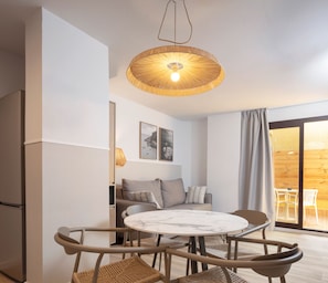 Ein modernes Wohnzimmer mit einem runden Marmortisch, Korbstühlen, einer Couch mit Kissen, einer Hängeleuchte und Blick durch eine Glastür.