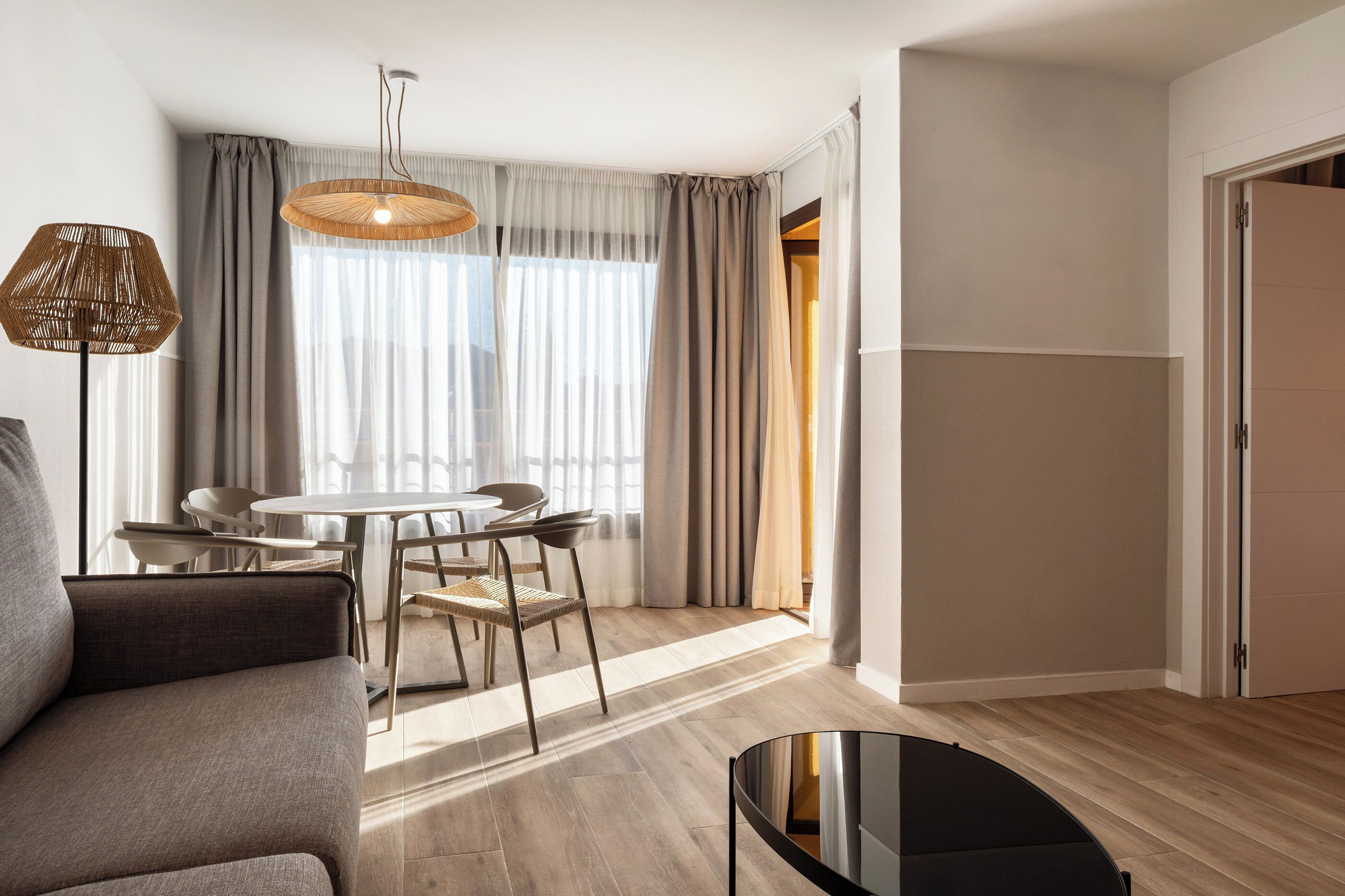 Un salon moderne comprenant un canapé, une table à manger, des chaises, un luminaire suspendu et une porte donnant sur une autre pièce.