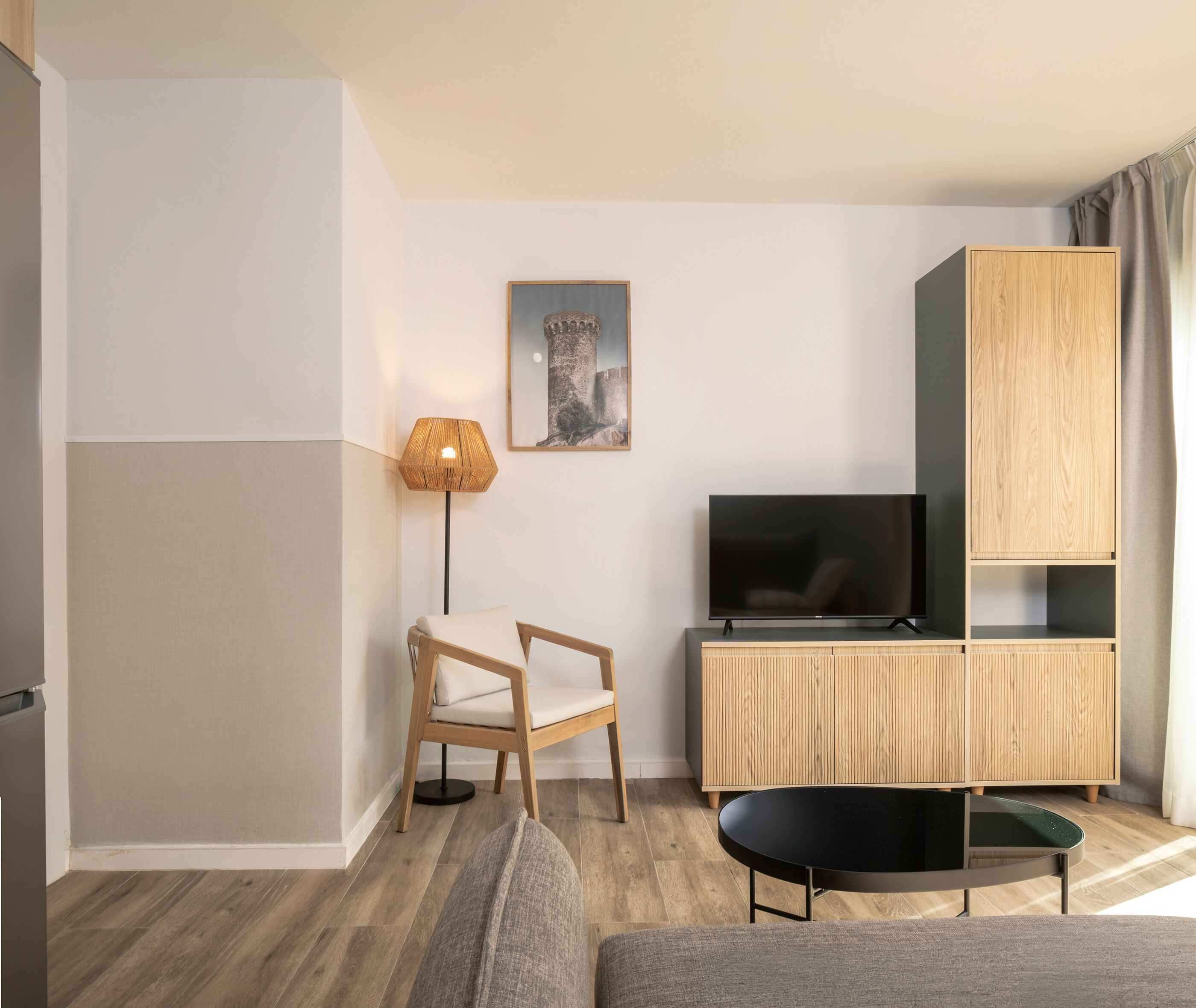 A modern living room with a TV, wooden cabinet, chair, lamp, and a sofa.