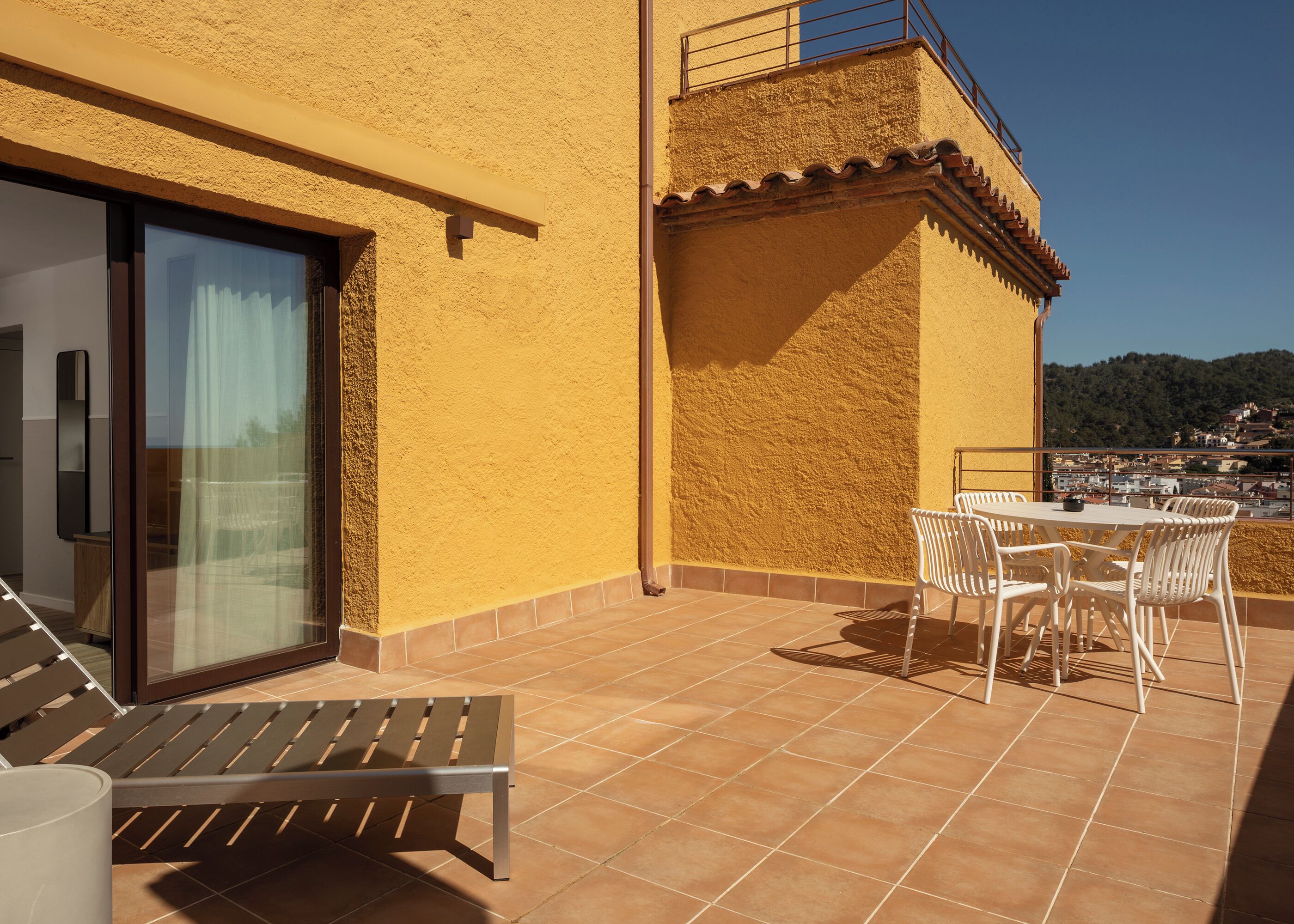 A terrace with a table and chairs, a bench, and a glass door leading to an interior space.