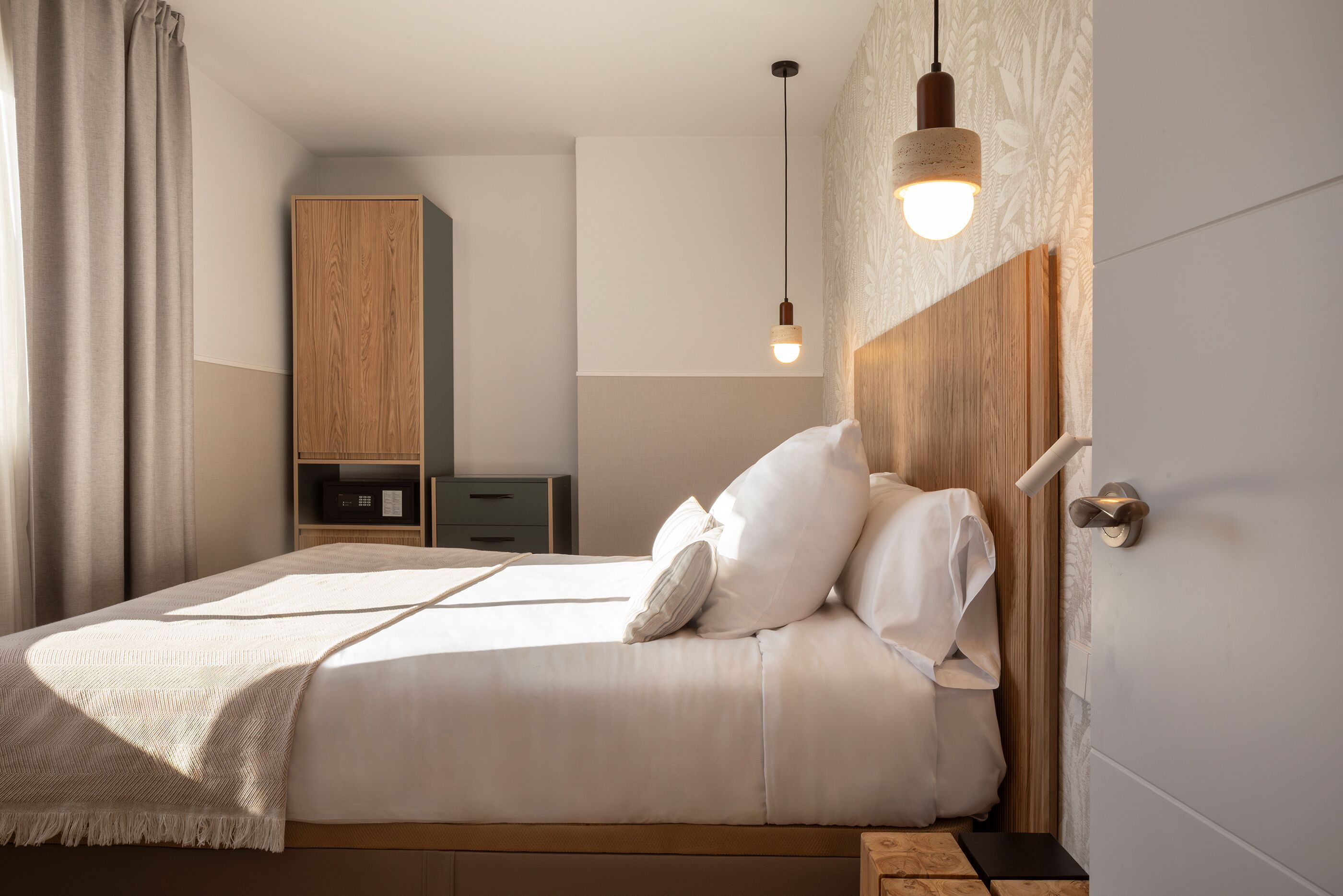 A neatly made bed with pillows, a hanging light fixture, and a wooden headboard.