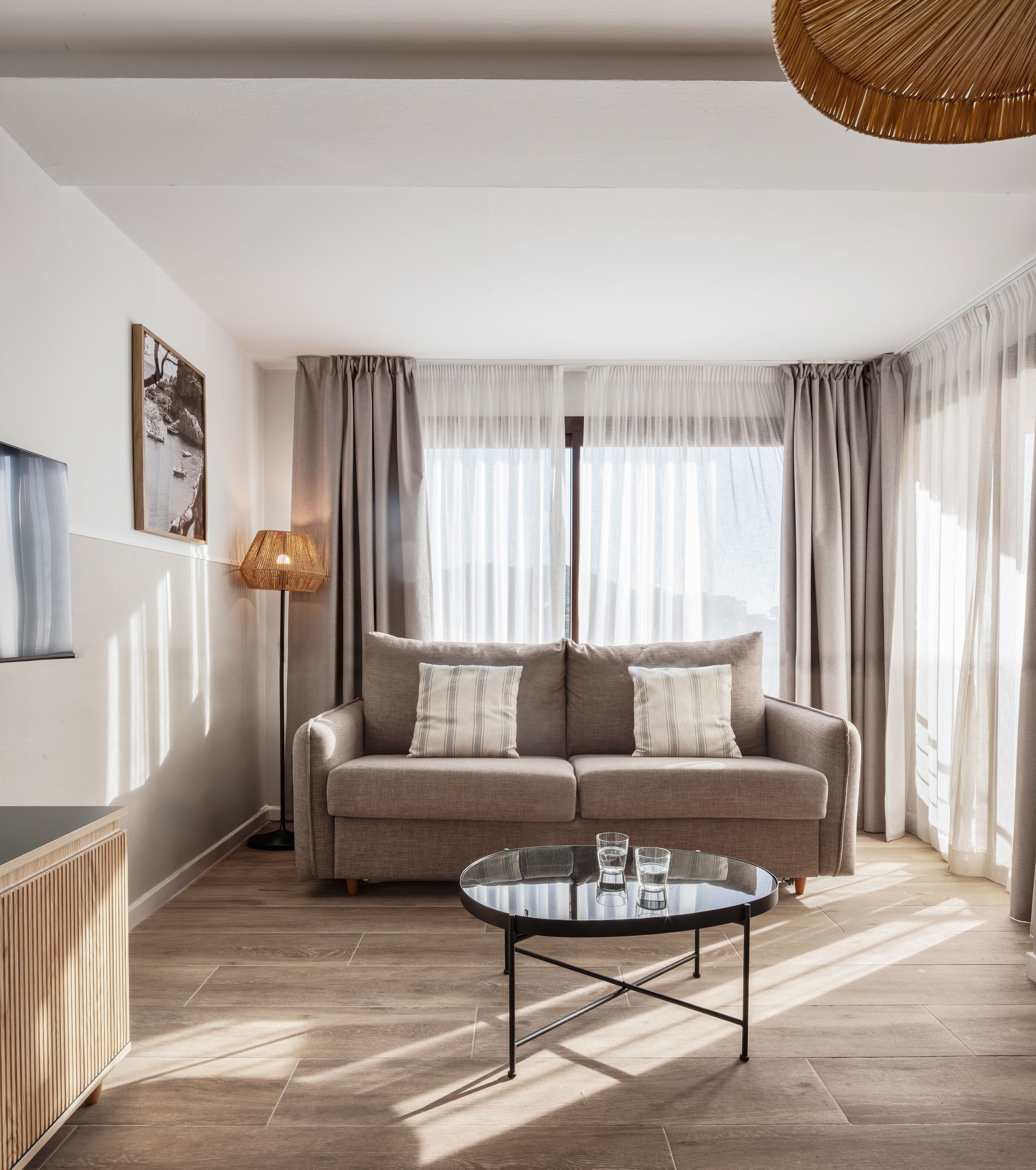 Un salon avec un canapé, une table basse, un lampadaire et des rideaux légers.