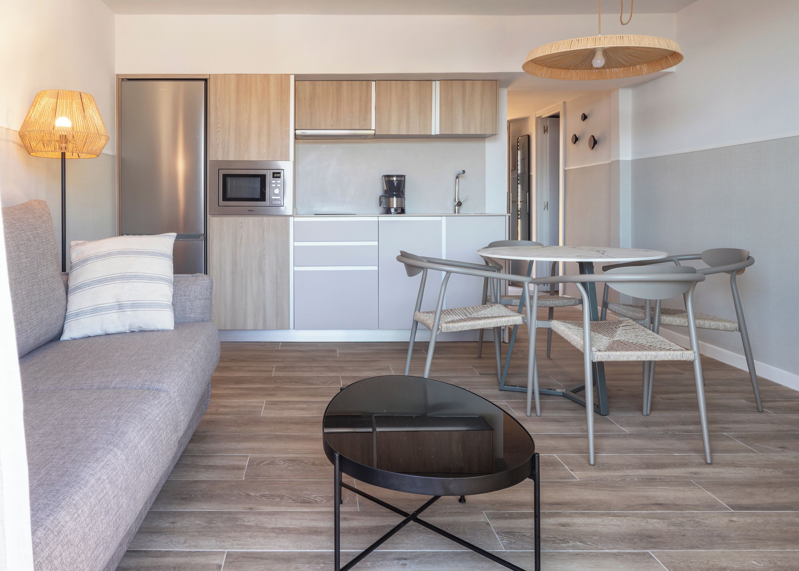 A modern kitchenette with a microwave, coffee maker, and cabinets. There is a dining area with a table and chairs.