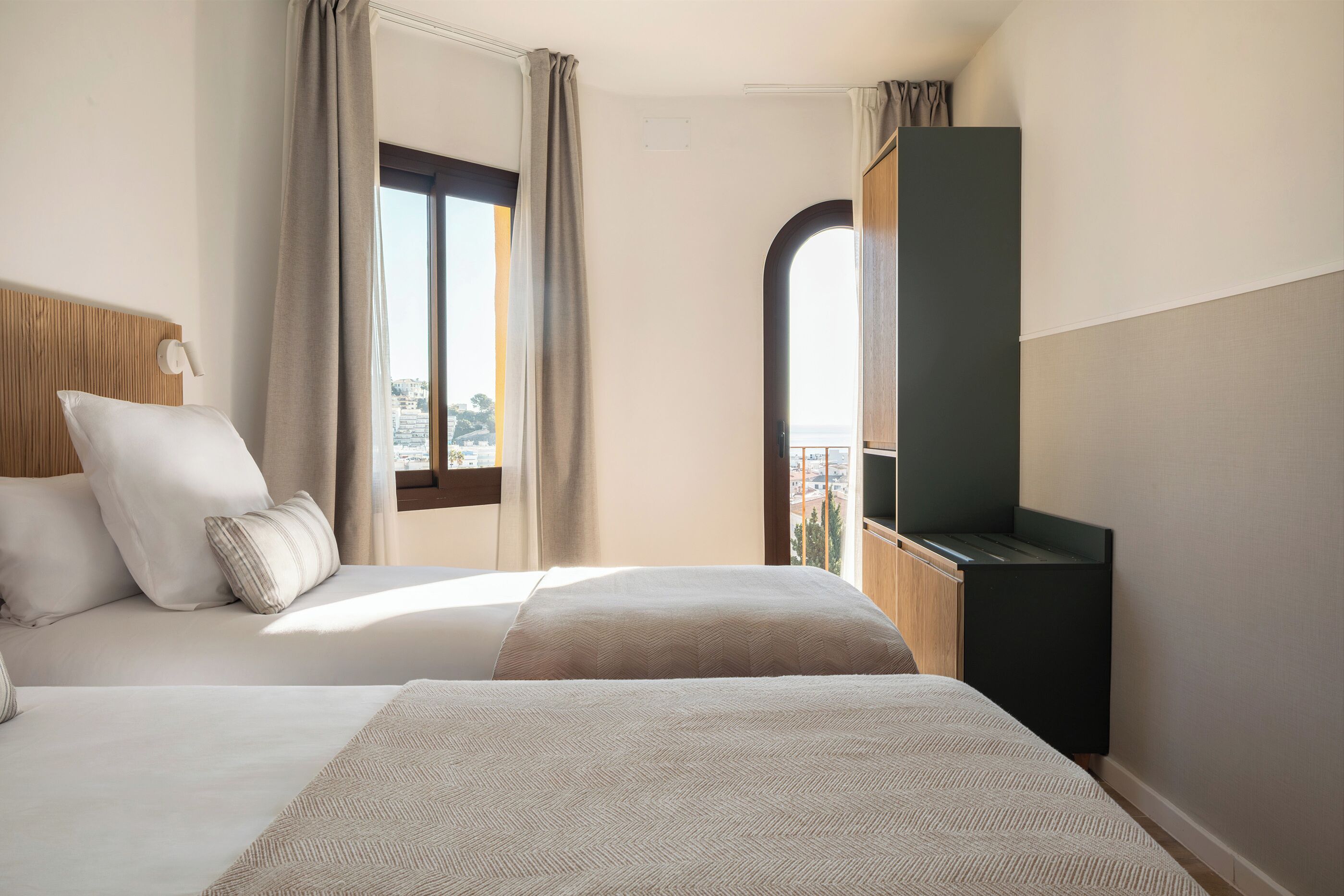 A hotel room with a bed, a TV, a window with curtains, and a view of the city.