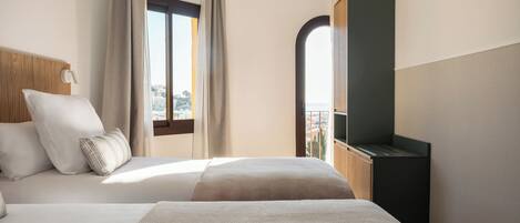 A hotel room with a bed, a TV, a window with curtains, and a view of the city.