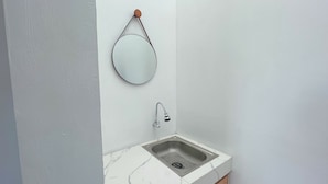 A bathroom with a white marble sink, a round mirror, and a faucet. - Sovilla II Yogyakarta (Depok)