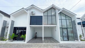 A modern two-story building with a flat roof, large windows, and a paved entrance area. - Sovilla II Yogyakarta (Depok)