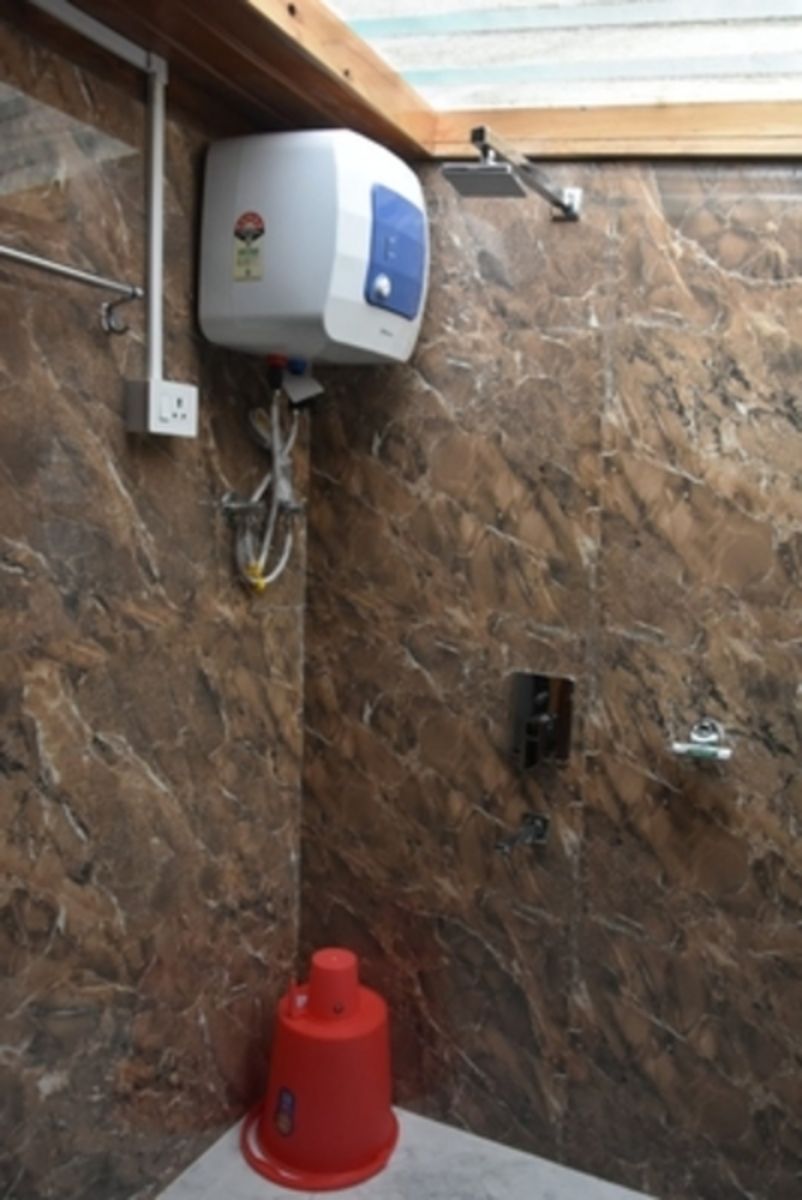 A bathroom with a marble wall, a water heater, and a red object on the floor.