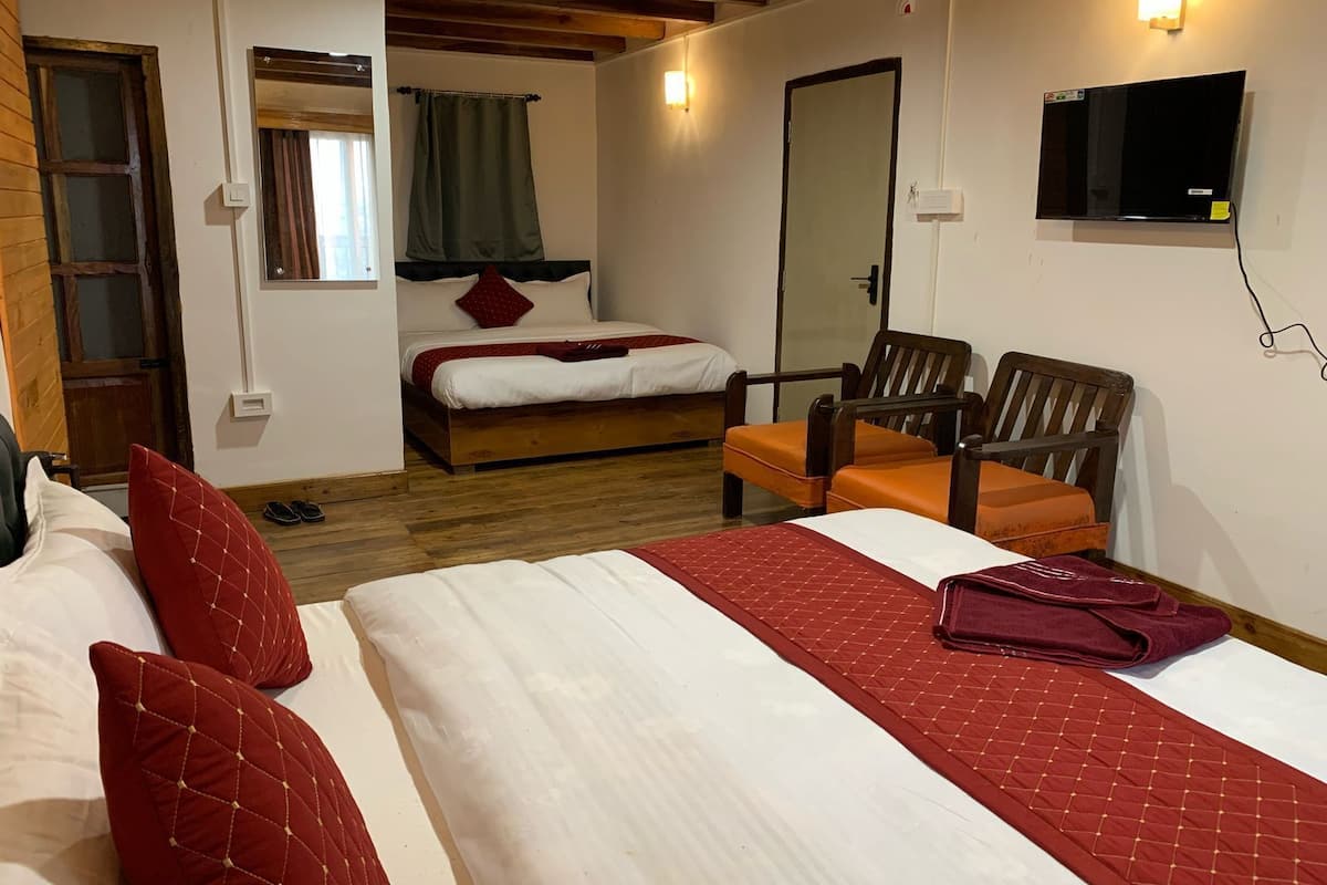 Habitación de hotel con dos camas, techo de madera, televisor montado en la pared y una silla con cojín naranja.
