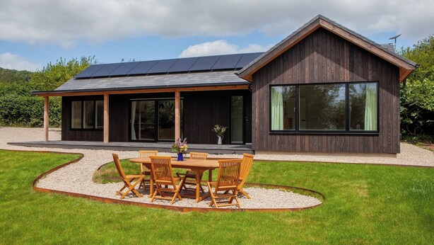 Una casa moderna con un amplio patio, un comedor con mobiliario de madera y un techo con paneles solares.