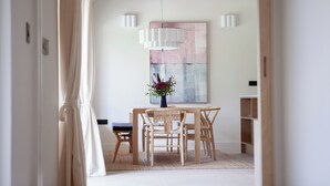 Un comedor con una mesa y sillas de madera, un jarrón con flores y un cuadro abstracto grande en la pared.