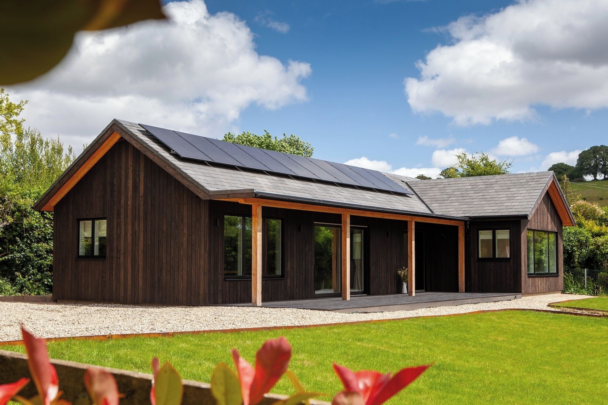 A modern wooden house with a sloped roof, large windows, and a covered porch area.
