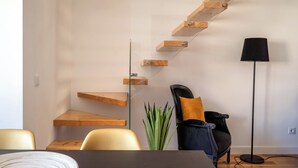 A modern interior with a wooden staircase, a black floor lamp, and a dining area with chairs and a table. - Masala Duplex Apartment, Penha de França, Lisbon (Lisboa)