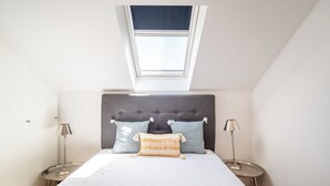 A bedroom with a bed, two nightstands, a window, and a skylight. - Masala Duplex Apartment, Penha de França, Lisbon (Lisboa)