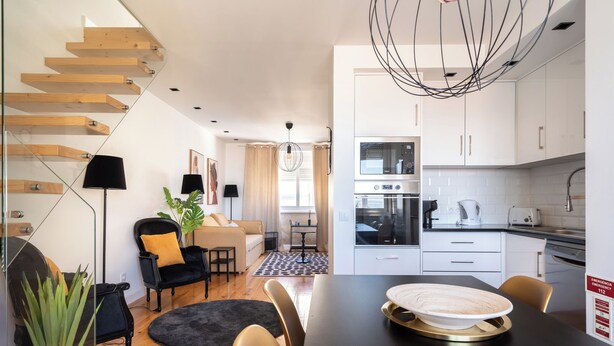 A modern kitchen with white cabinets, a built-in oven, and a dining area with a black table and chairs. - Masala Duplex Apartment, Penha de França, Lisbon (Lisboa)