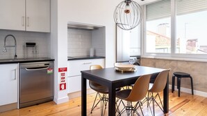 A modern kitchen with white cabinets, a stainless steel dishwasher, and a dining area with a black table and chairs. - Masala Duplex Apartment, Penha de França, Lisbon (Lisboa)