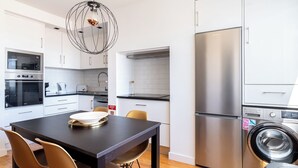 A modern kitchen with white cabinets, stainless steel appliances, a dining table with chairs, and a washing machine. - Masala Duplex Apartment, Penha de França, Lisbon (Lisboa)