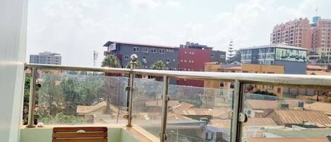 A balcony with a wooden bench, glass railing, and a view of surrounding buildings.